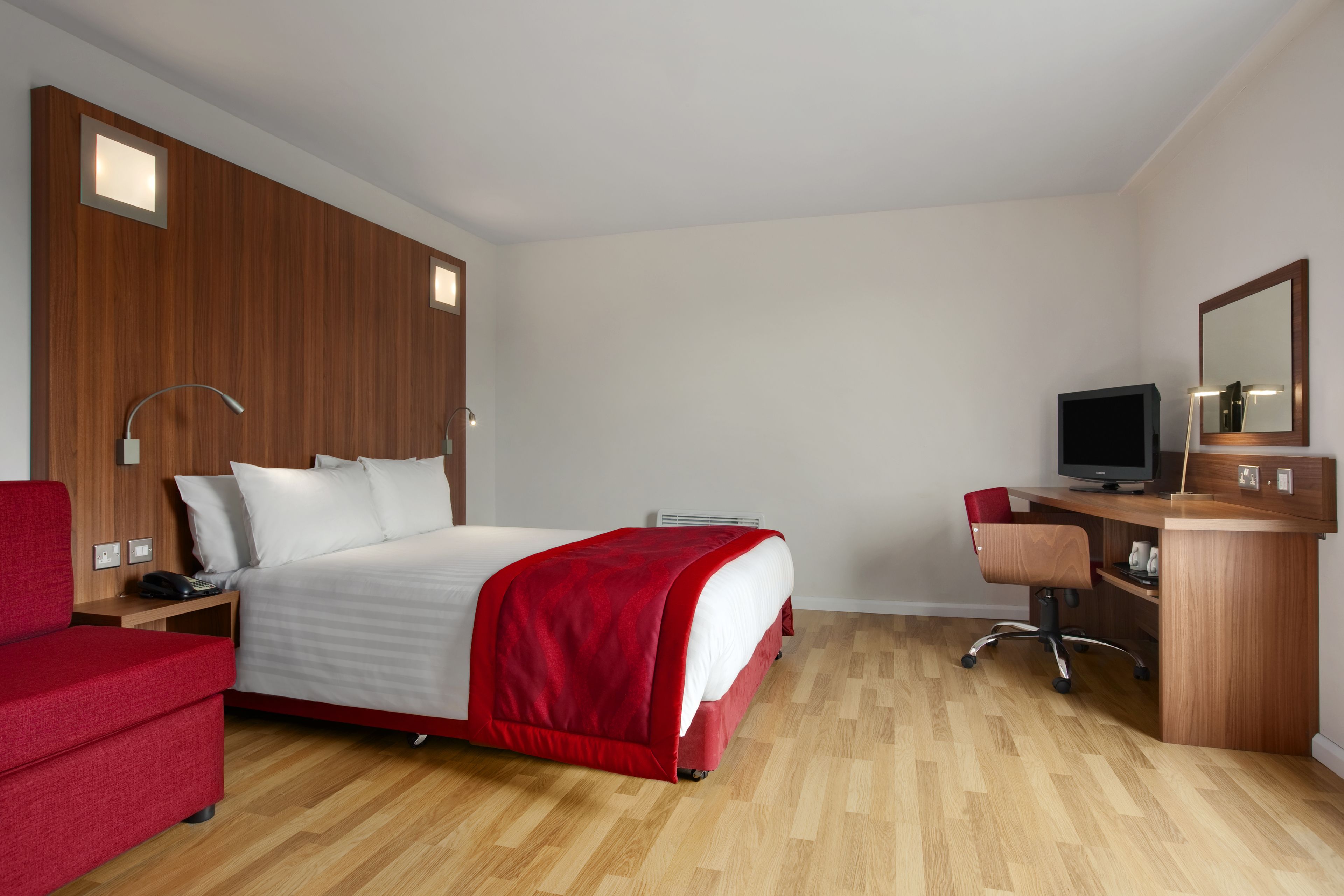 A hotel room with a bed, a desk, a chair, a TV, and a mirror.