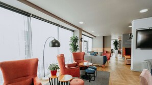 A modern living room with red armchairs, a sofa, and a TV. There are plants and a floor lamp. - Ramada Encore by Wyndham Newcastle-Gateshead (Gateshead)