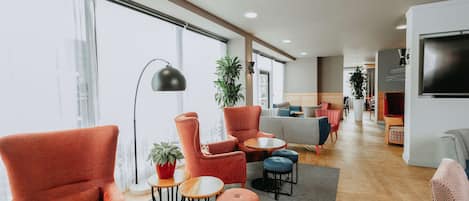 A modern living room with red armchairs, a sofa, and a TV. There are plants and a floor lamp.