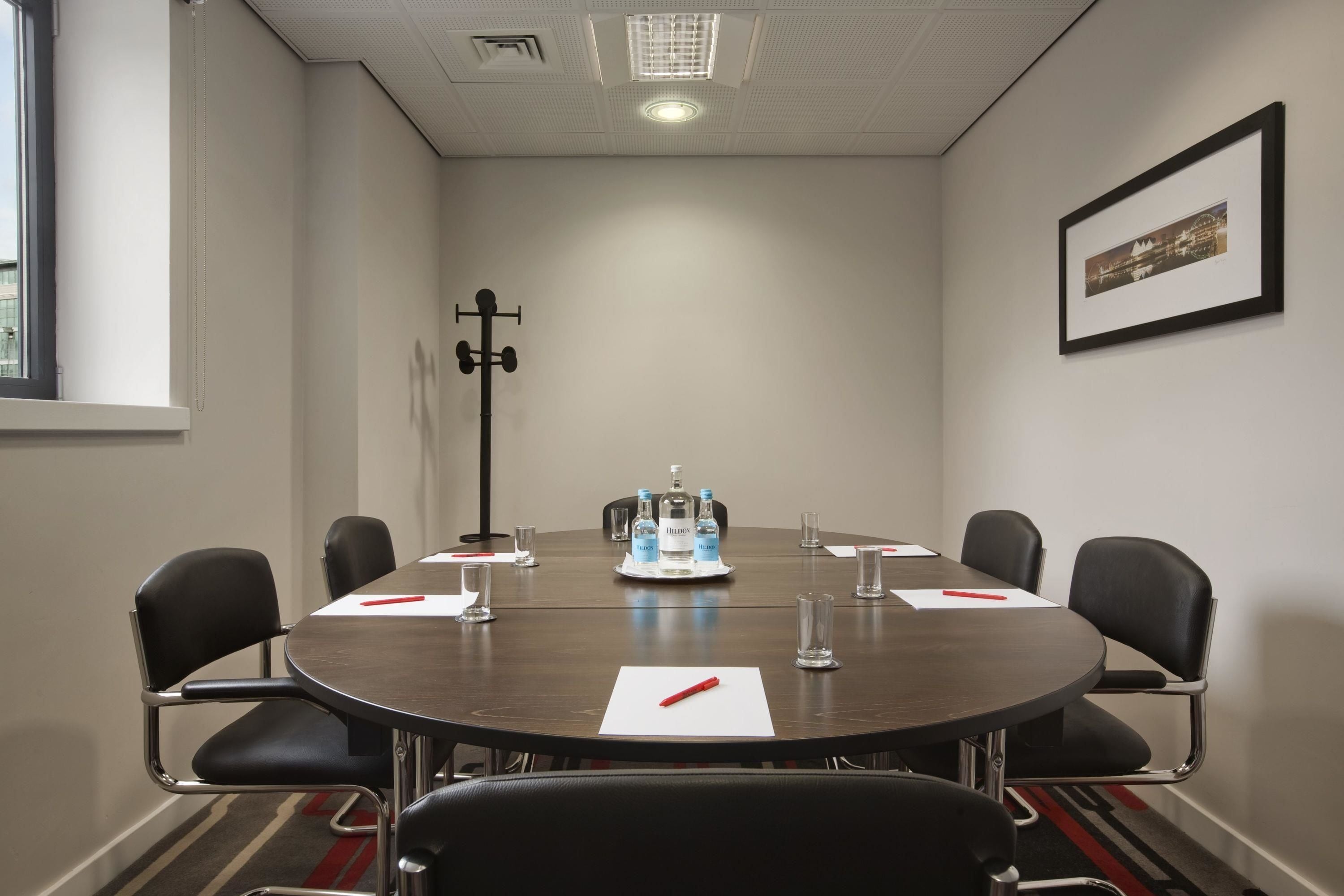 A conference room with a round table, black chairs, water bottles, and a framed picture on the wall.