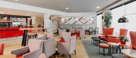 A modern lounge area with seating arrangements, a bar, and a decorative wall.