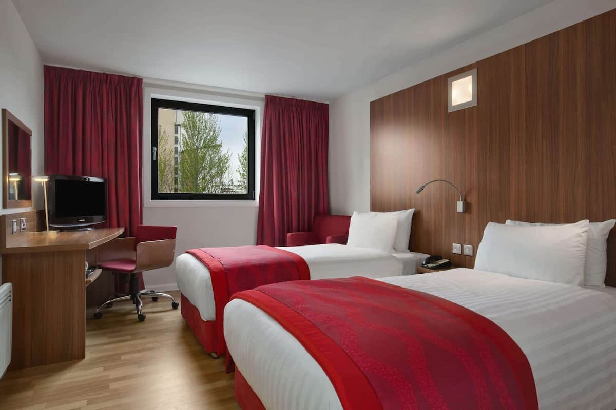 A hotel room with two beds, a desk, a TV, and a window with curtains.