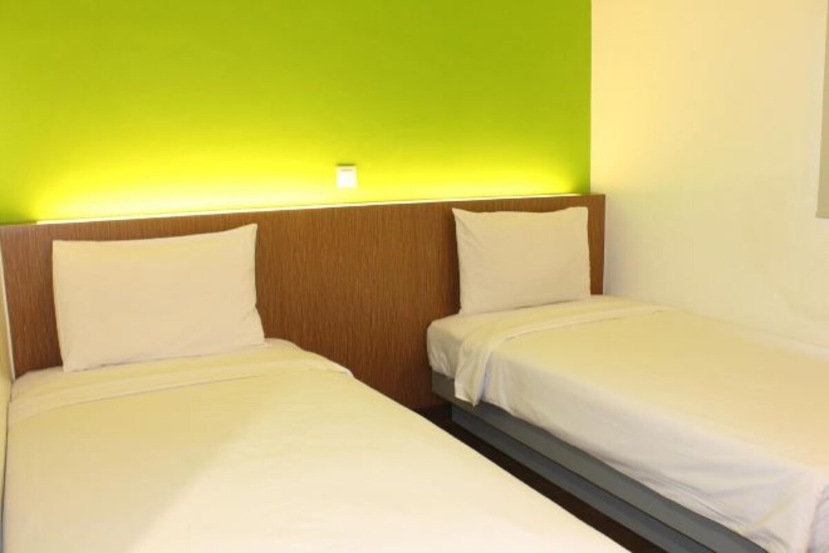 A hotel room with two single beds, a wooden headboard, and a green wall.