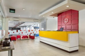 A modern reception area with a yellow and white desk, red seating, and an exit sign. - Amaris Hotel Pemuda Semarang (Semarang)