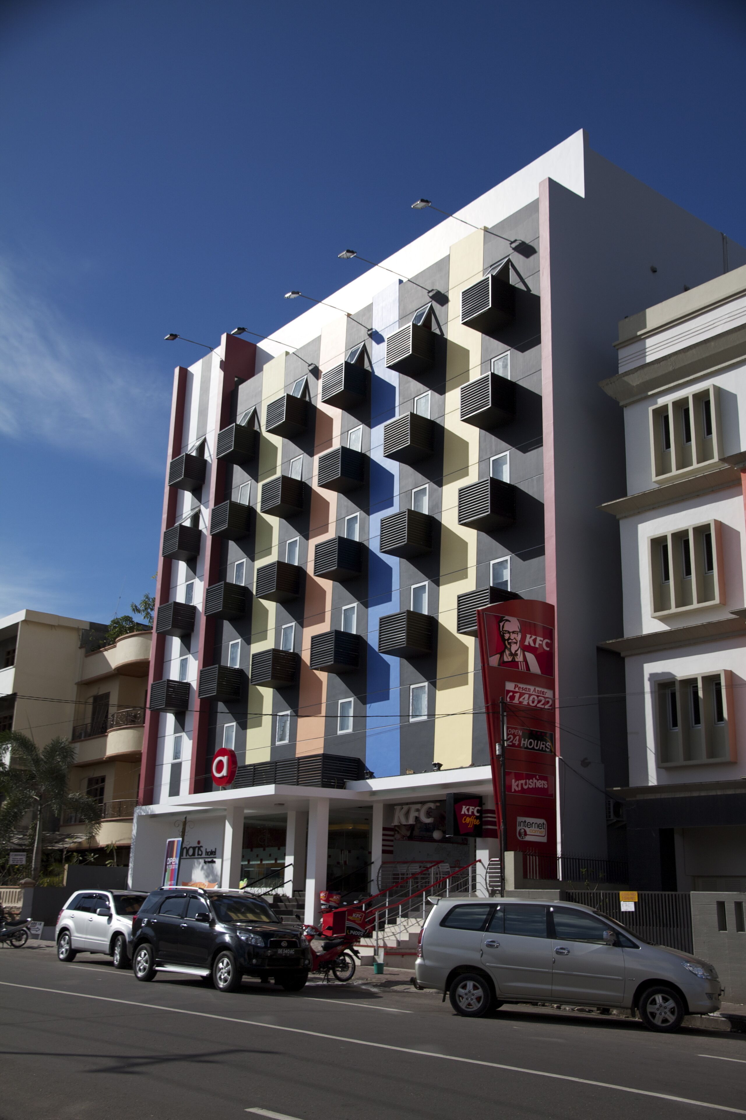 A multi-story building with balconies, a KFC restaurant, and a sign for a 24-hour house.