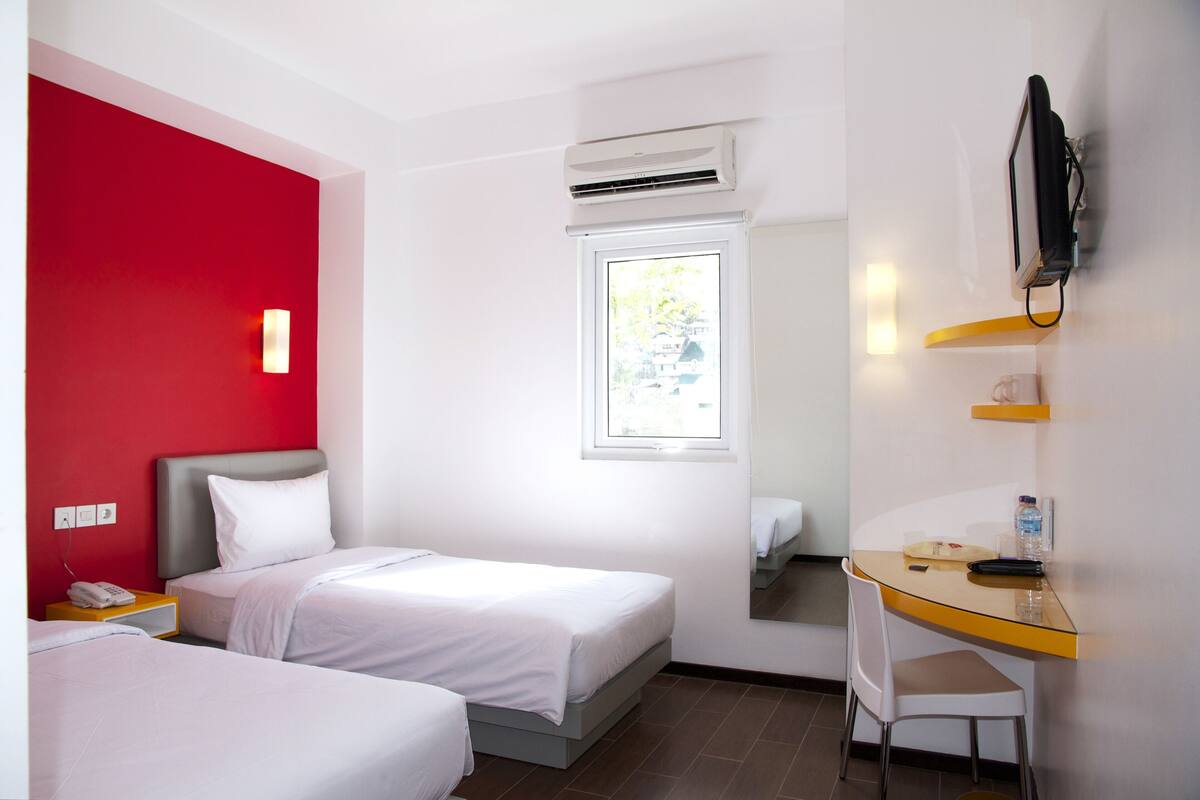 A hotel room with two beds, a desk, a chair, a TV, and a window.