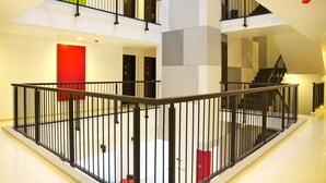 A modern interior with a central open space, multiple staircases, and a red accent wall. - Amaris Hotel Ambon (Ambon)