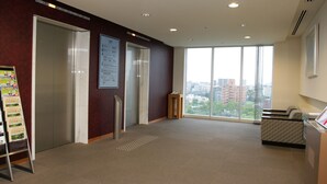 Un hall d’entrée spacieux avec un plafond haut, un comptoir d’accueil, un espace salon et une vue sur la ville grâce à de grandes fenêtres.