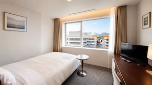 Habitación de hotel con cama, una mesita, televisor y ventana con vistas a la ciudad.