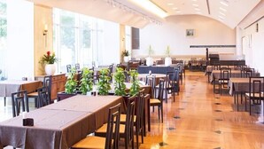 Un grand espace dédié à la salle à manger, avec de longues tables, des chaises et des plantes en pot.