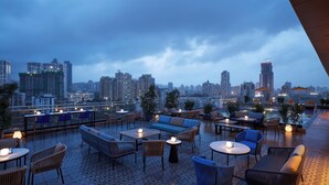A rooftop terrace with seating areas, tables, and a pool, overlooking a cityscape with high-rise buildings. - Vivanta Thane LBS Road (Thane)