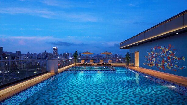 A rooftop pool with a city view, lounge chairs, and a decorative wall. - Vivanta Thane LBS Road (Thane)