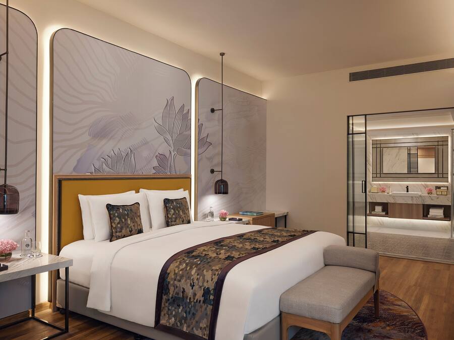 A modern hotel room with a large bed, bedside tables, a desk, and a bathroom with a mirror and sink.