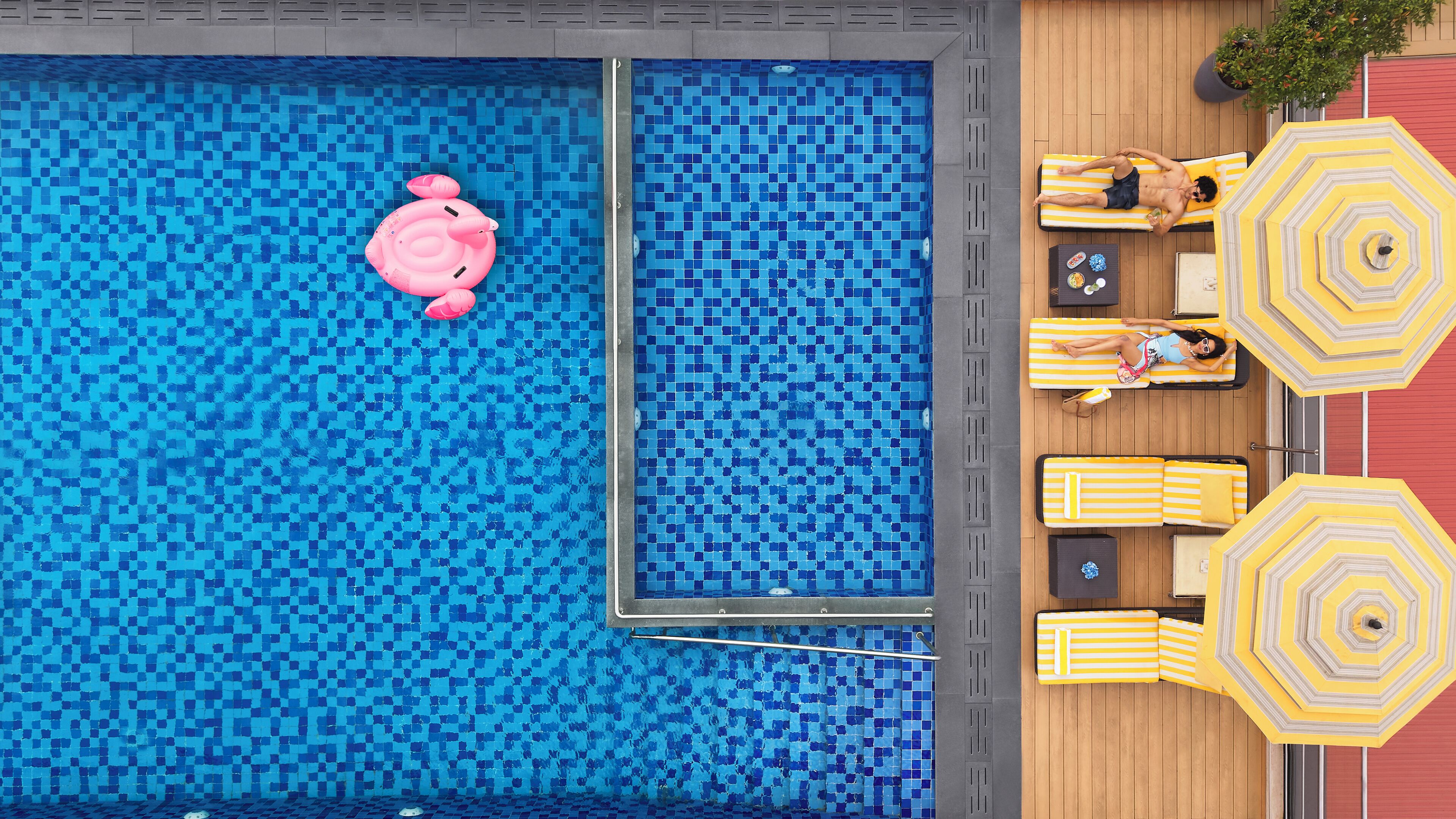 En pool på taket med en rosa badmadrass, solstolar med gula ränder och parasoller.