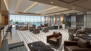 A spacious lobby with a modern design, featuring a large seating area, a bar, and large windows offering a view of the ocean. - Vivanta Thane LBS Road (Thane)