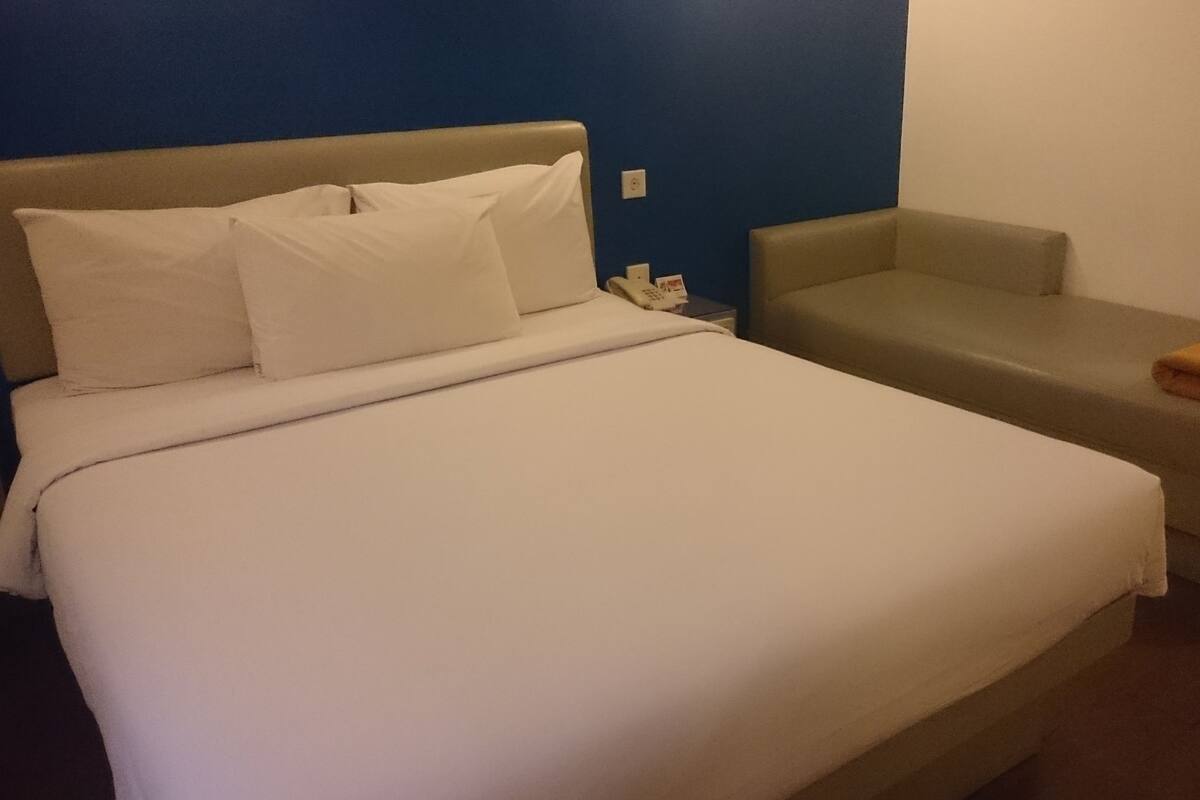 A hotel room with a bed, a small sofa, and a nightstand with a phone.