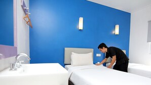 A hotel room with a blue accent wall, a bed with white bedding, a bedside table, a sink, and a mirror.