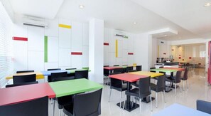 A modern dining area with multiple tables and chairs, white walls, and colorful vertical accents.