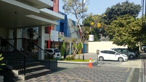 A modern building with a staircase leading to a gated entrance, a parking area, and a tree with yellow flowers.