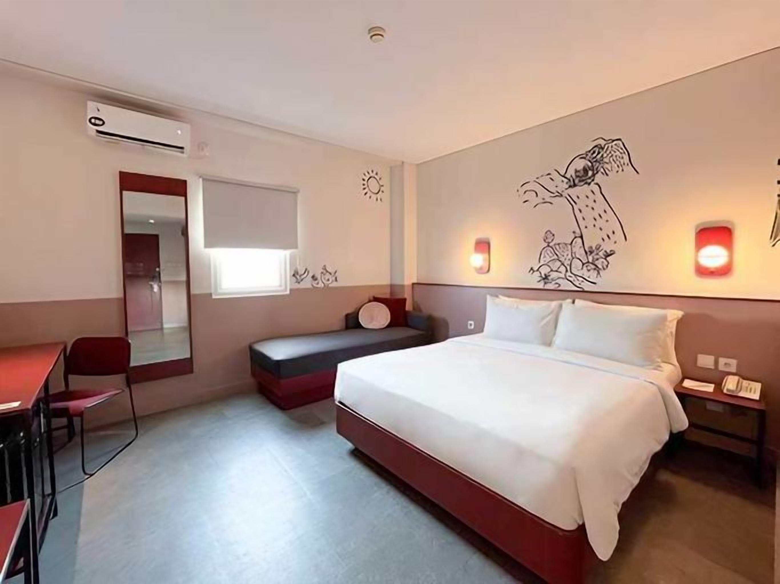 A hotel room with a bed, a desk, a chair, a mirror, and wall-mounted lights.