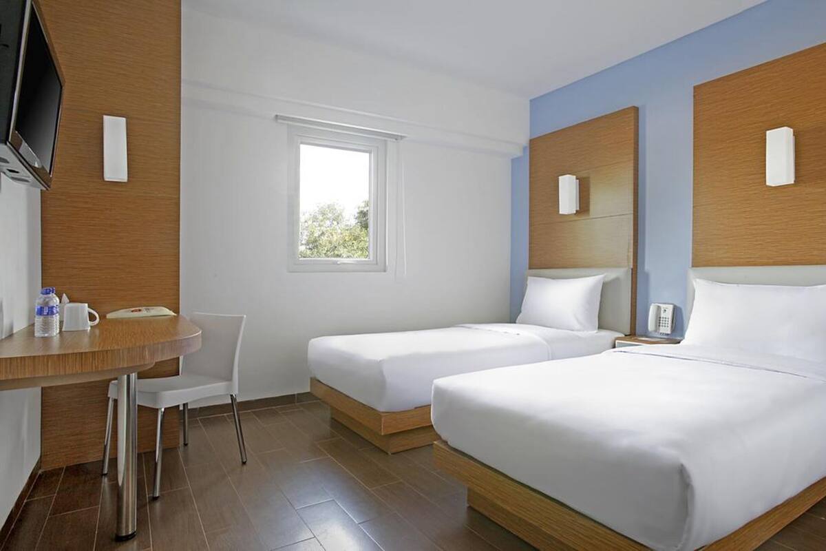 Una habitación de hotel con dos camas, un escritorio con una silla, un televisor y una ventana.