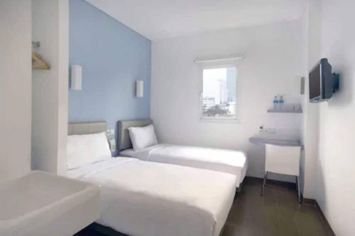 Habitación de hotel con dos camas, una ventana pequeña, un lavamanos y un televisor.