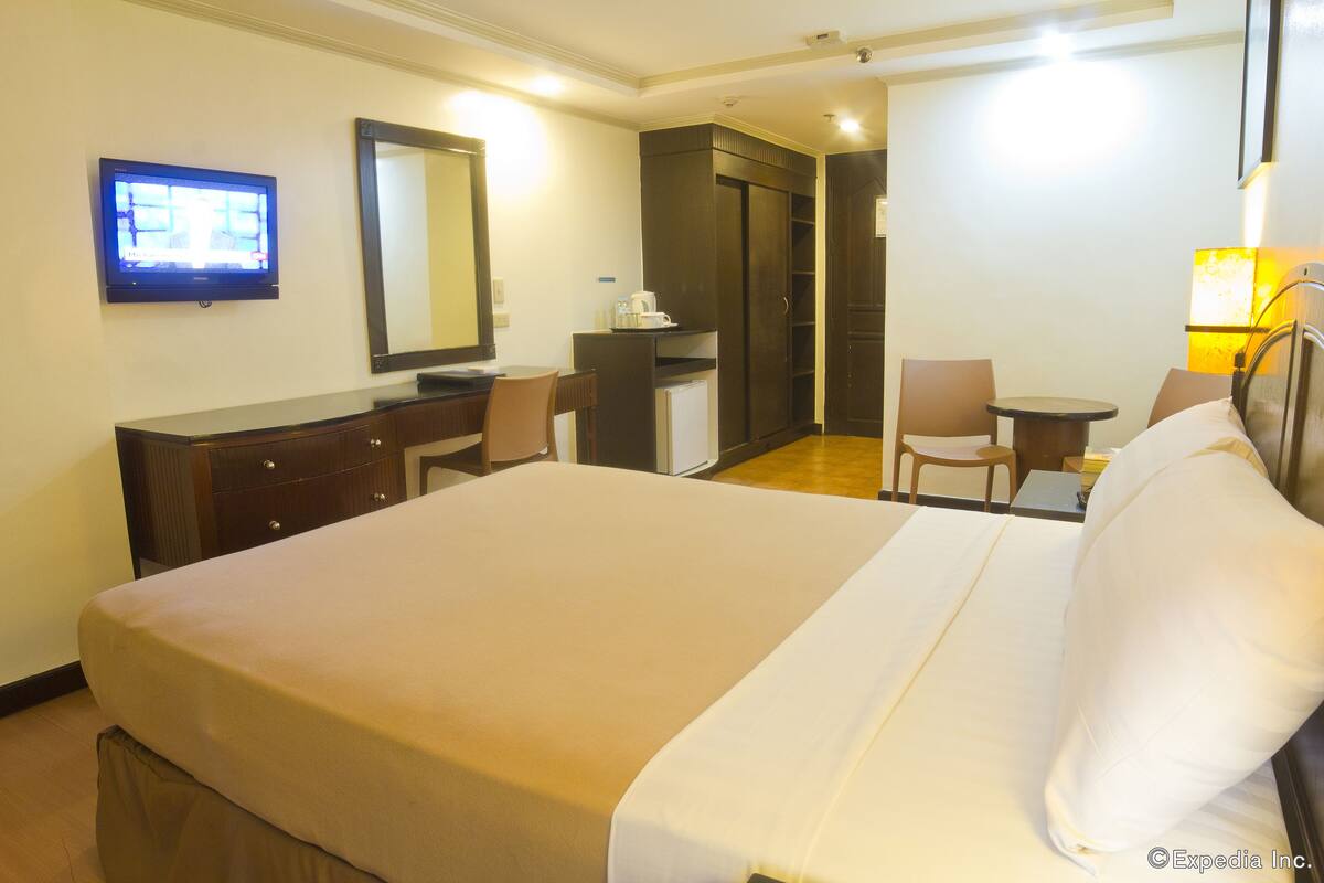 Una habitación de hotel con cama, escritorio, silla, televisor y espejo.