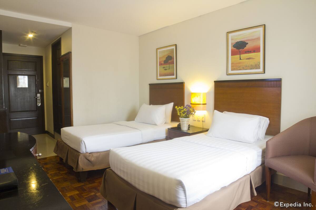 Una habitación de hotel con dos camas individuales, un escritorio, una silla y una puerta.