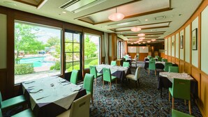 A hotel dining area with tables set for guests, large windows offering views of a pool and greenery, and a patterned carpet.