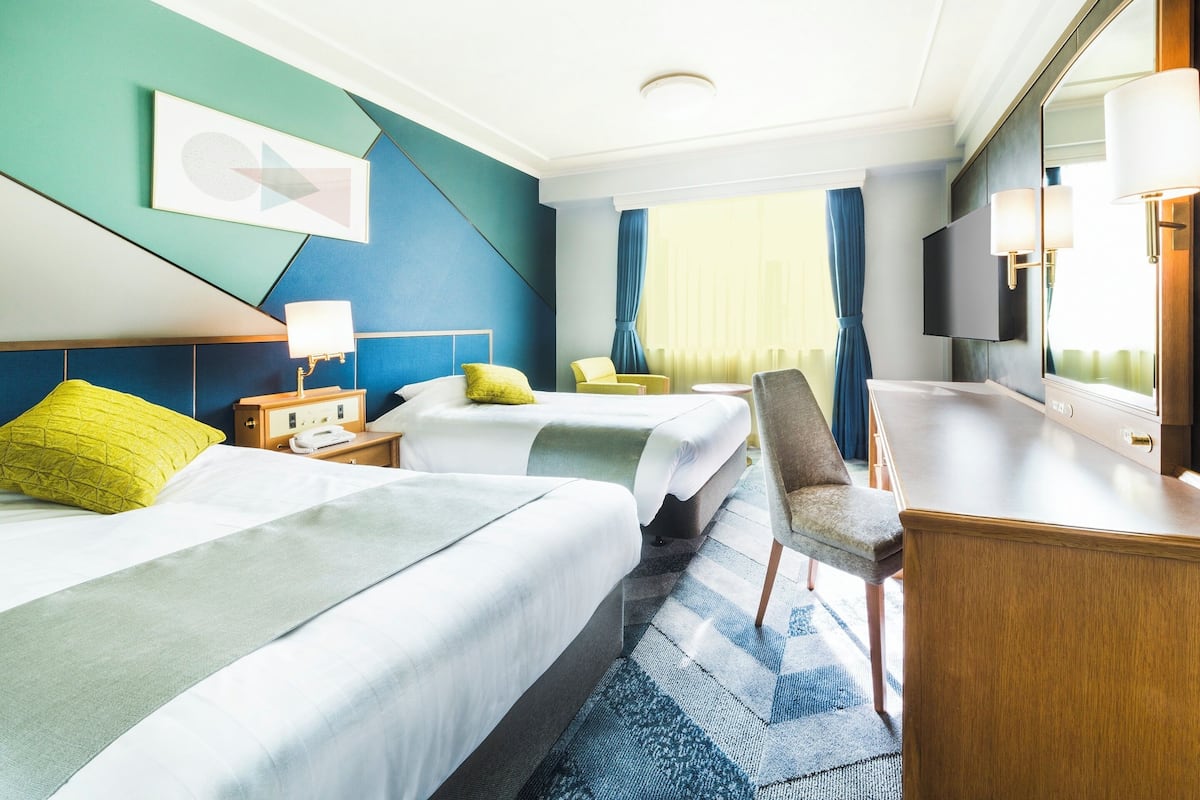 Une chambre d’hôtel avec deux lits, un bureau, une chaise, une télévision et un grand miroir.