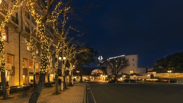 A hotel with a modern facade, a spacious courtyard, and a tree adorned with lights.