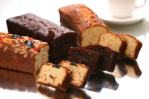 A loaf of bread with nuts and raisins, a loaf of dark bread, and slices of white bread on a reflective surface.
