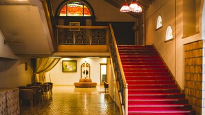 A staircase with red steps leading to a balcony, a dining area with chairs and a table, and a stained glass window above.