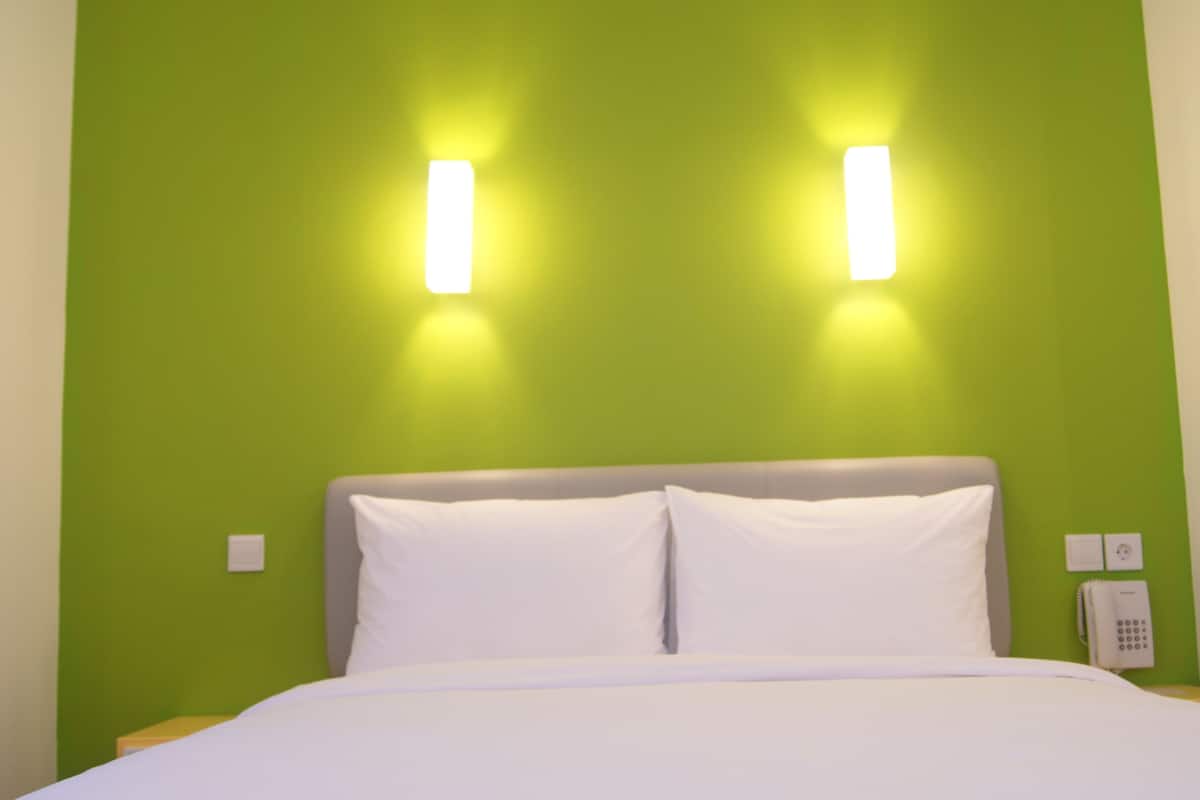A hotel room with a green wall, a white bed, and two wall-mounted lights.