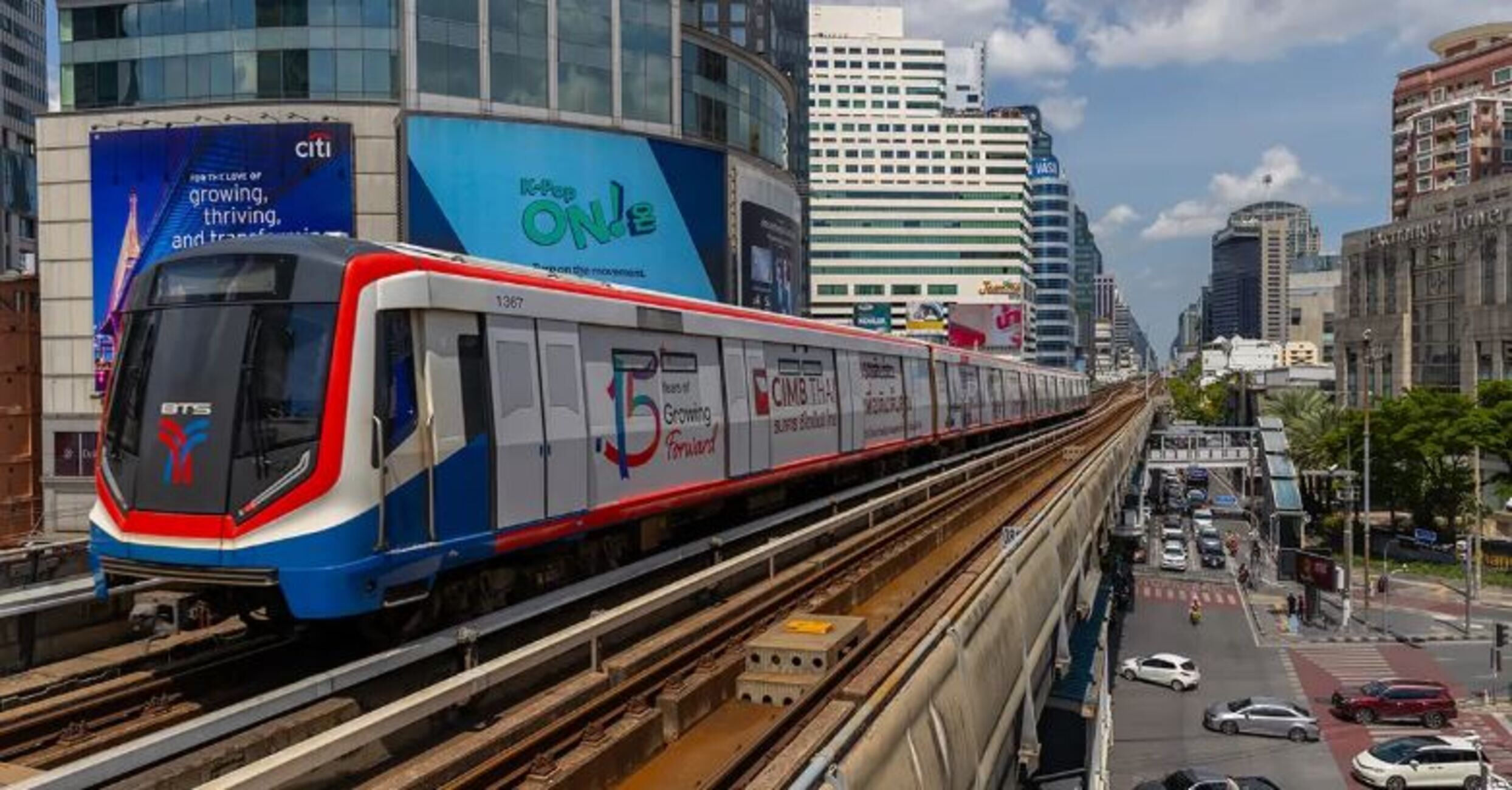 Een trein met reclame voor Citi en ONLE, rijdend door een stad met hoge gebouwen en een drukke straat.