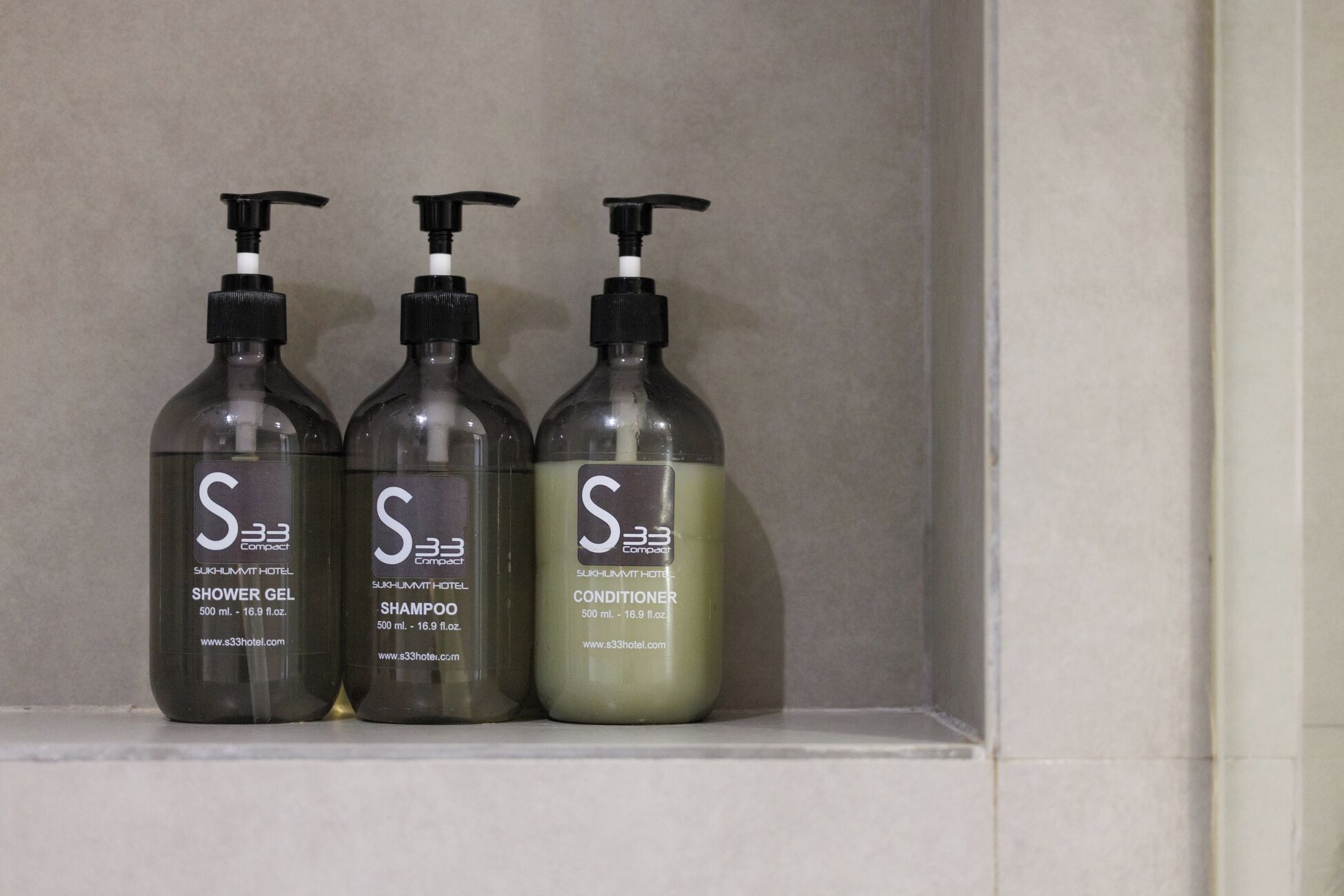 Three bottles of S33 Compact hotel toiletries on a shelf.