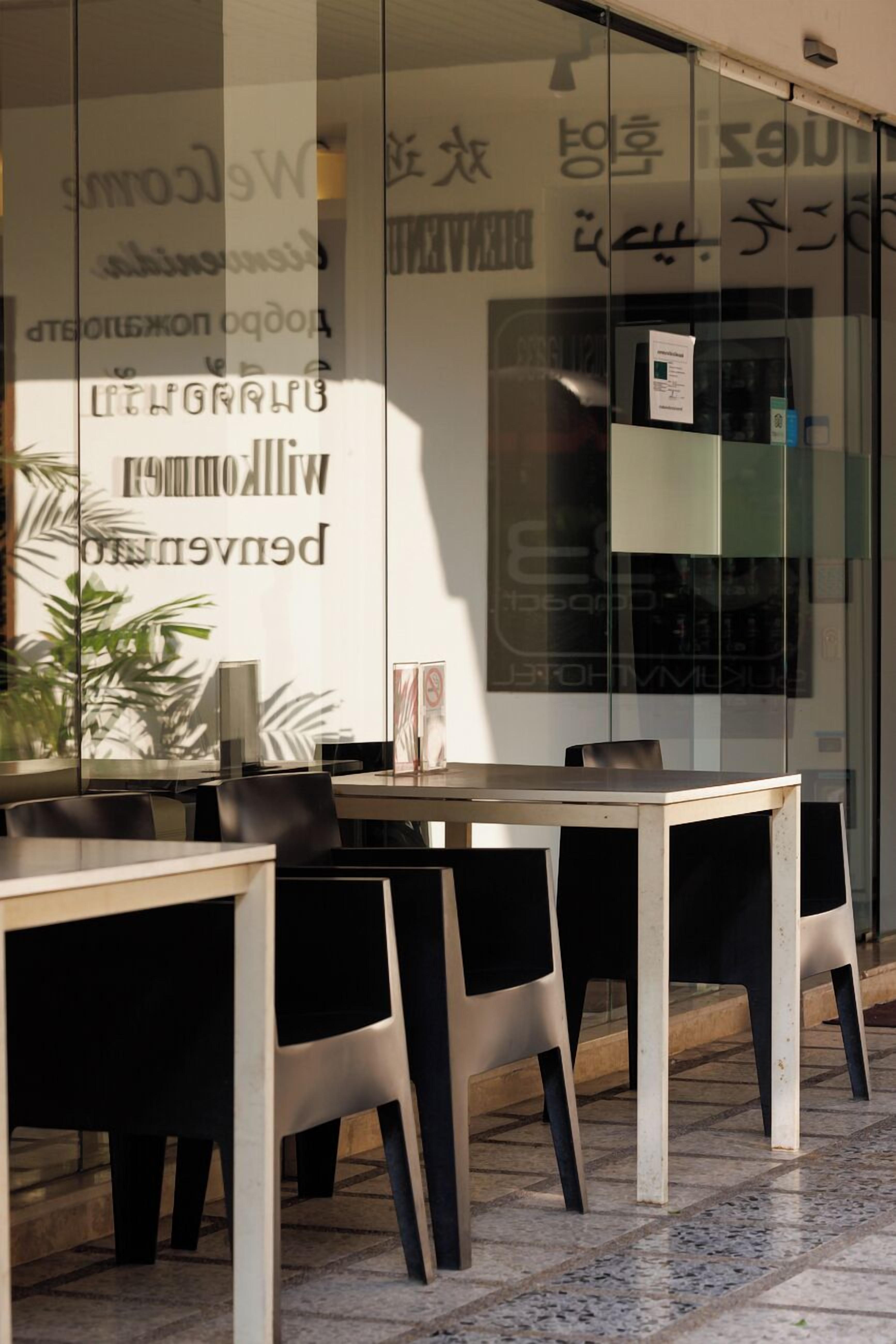 A modern interior with a glass wall displaying various text and logos, a wooden table, and black chairs.