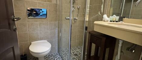 A bathroom with a glass-enclosed shower, a toilet, a sink with toiletries, and patterned floor tiles.