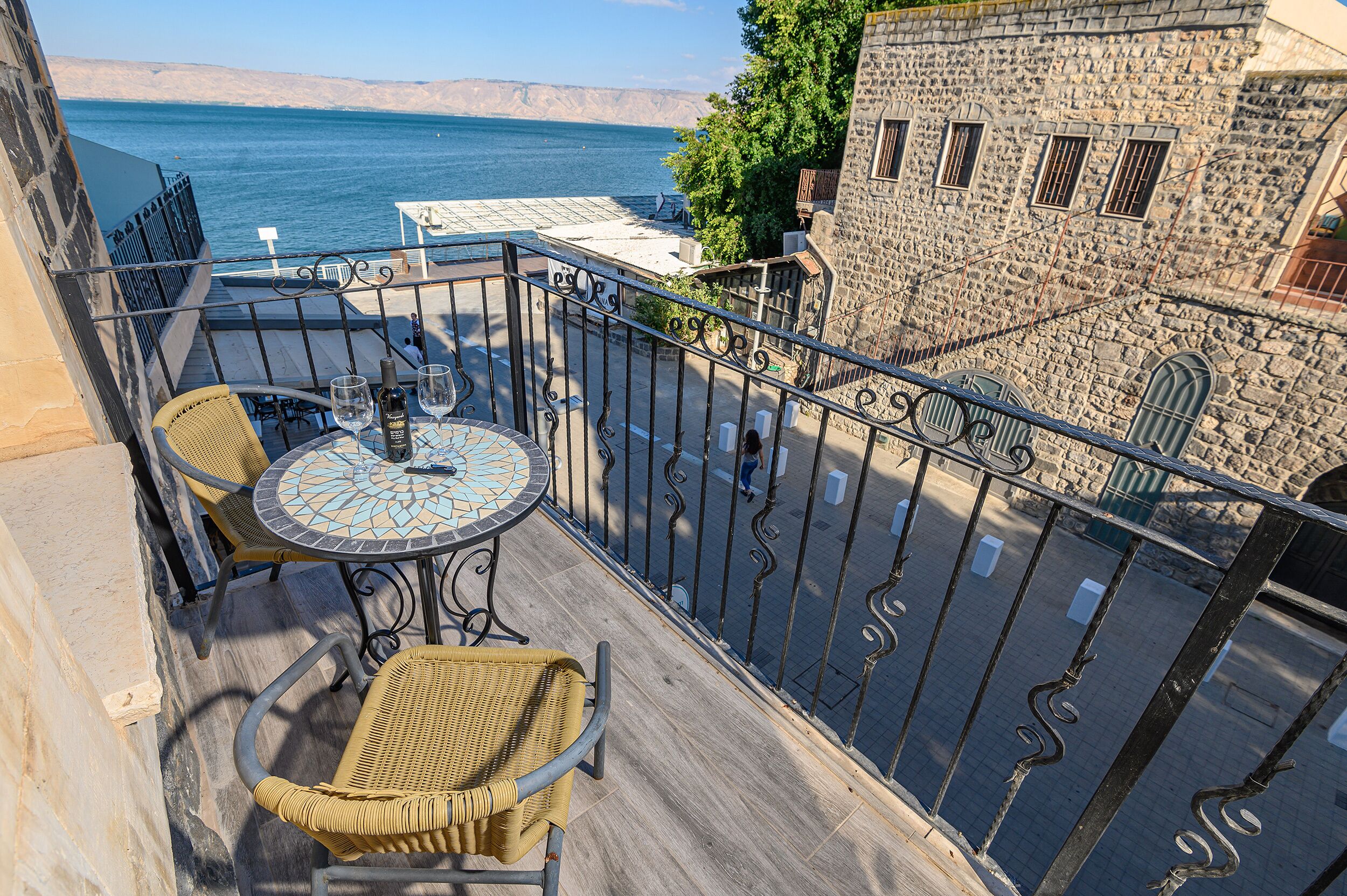 Un balcon avec des fauteuils en osier et une table, d’où l’on peut admirer un plan d’eau et un bâtiment en pierre.