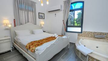 Une chambre à coucher comprenant un lit, des tables de chevet, une fenêtre avec des rideaux, une baignoire et un climatiseur fixé au mur.