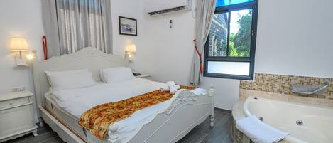 A bedroom with a bed, bedside tables, a window with curtains, a bathtub, and a wall-mounted air conditioner.