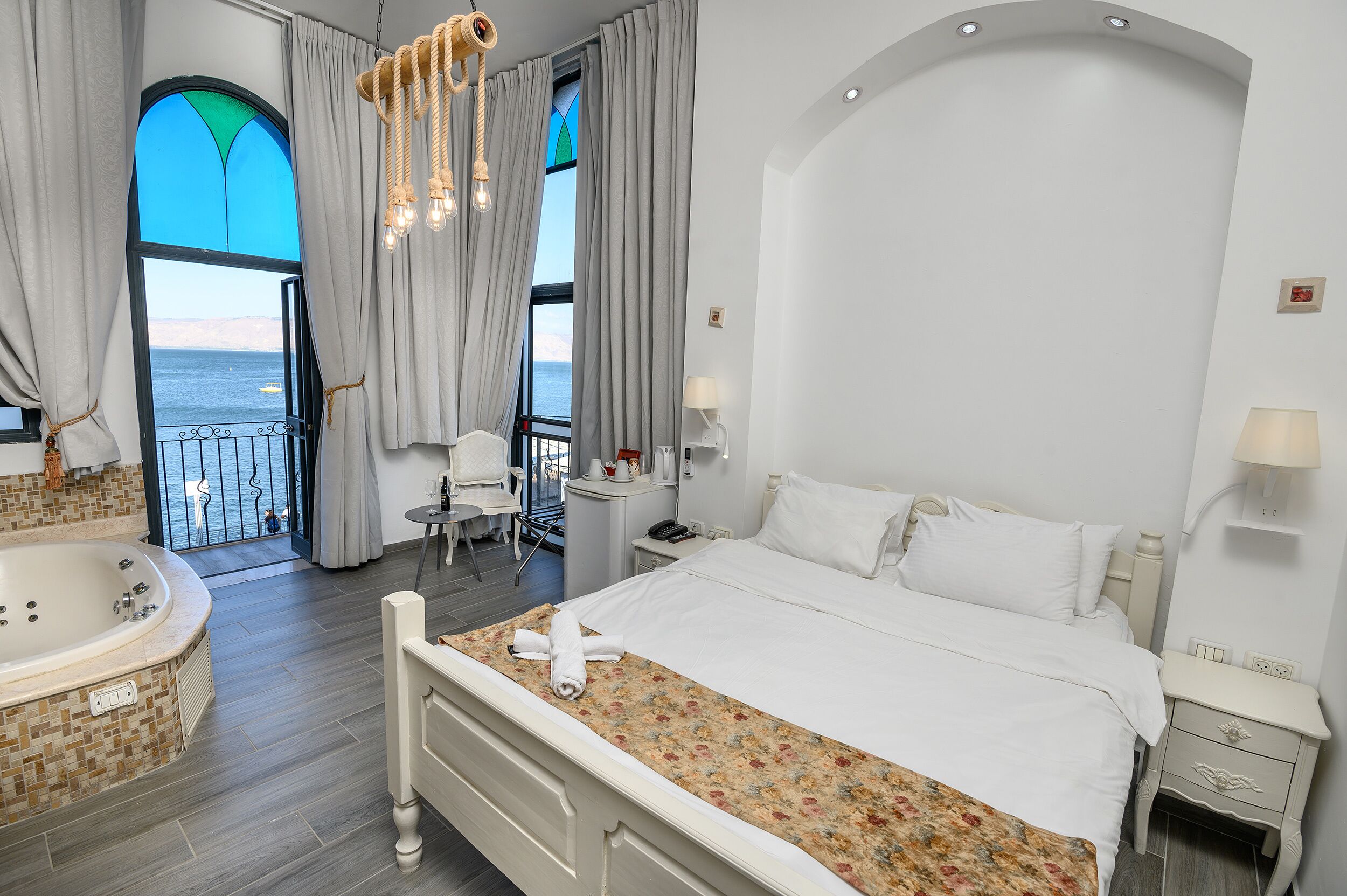 A bedroom with a large bed, a bathtub, and a view of the sea.