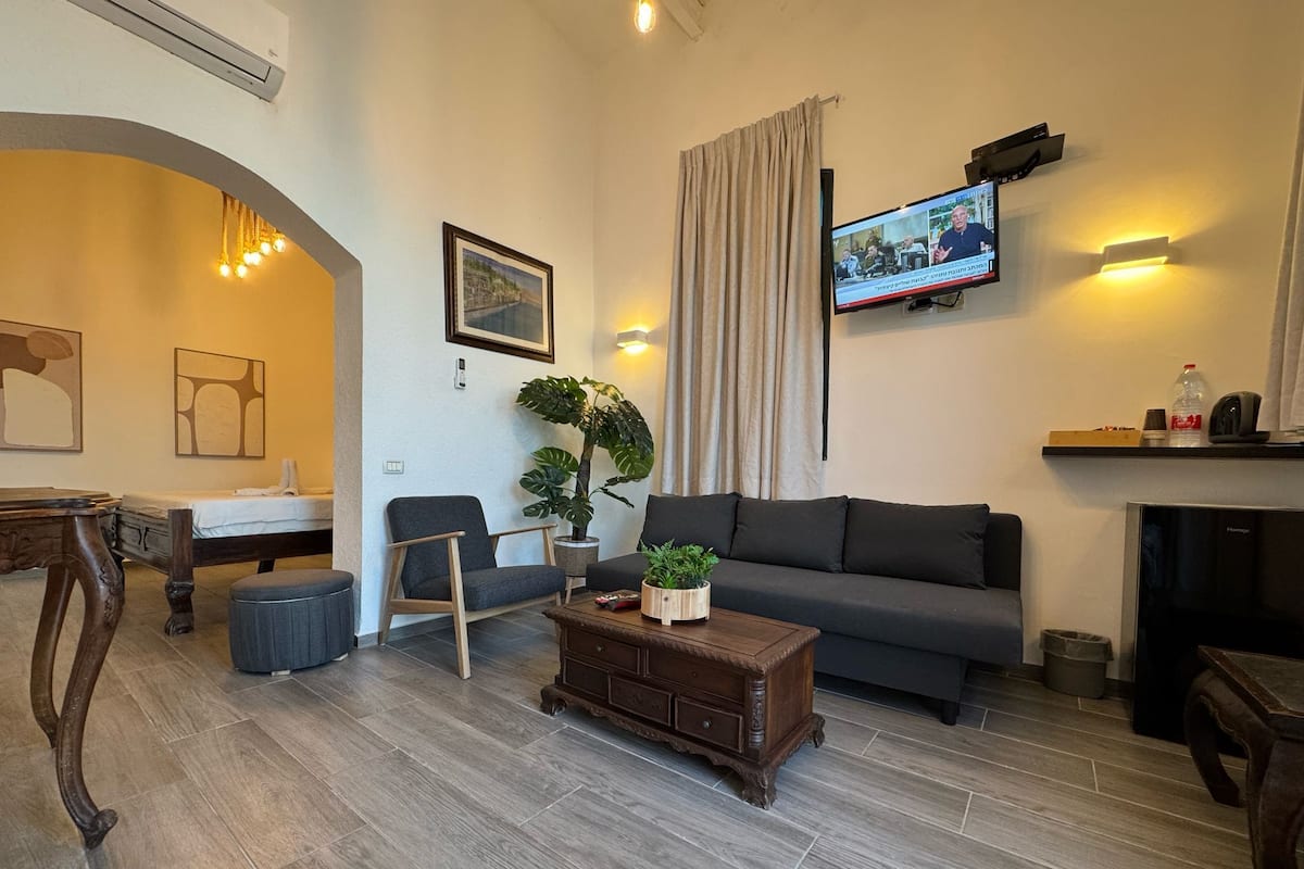 A modern living room with a grey sofa, a wooden coffee table, a TV mounted on the wall, and a potted plant.