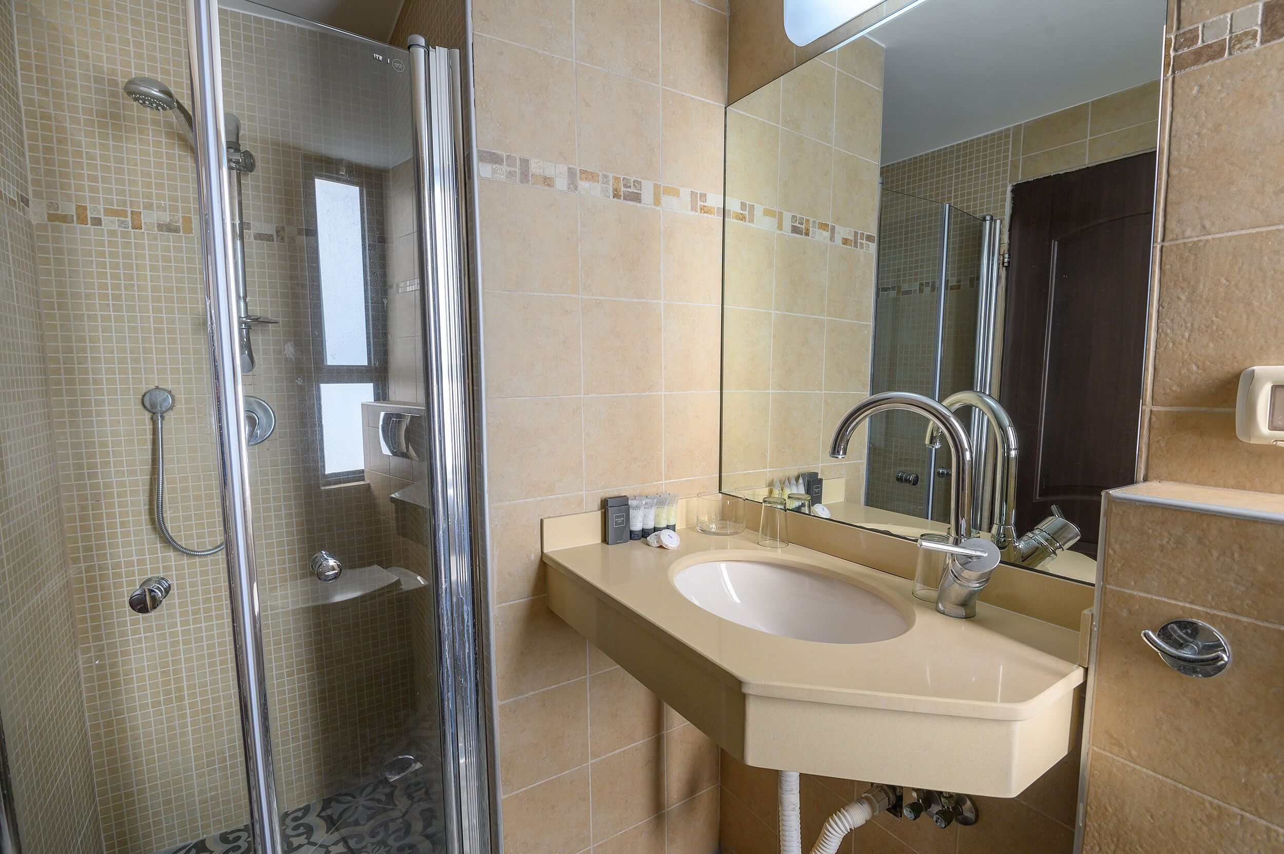 A bathroom with a glass shower enclosure, a sink with a mirror, and tiled walls.