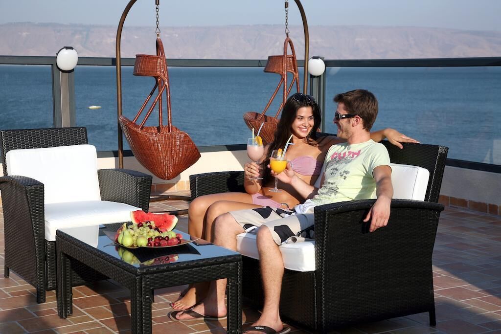 A couple relaxing on wicker furniture with a table of fruit and drinks in front of a scenic view.