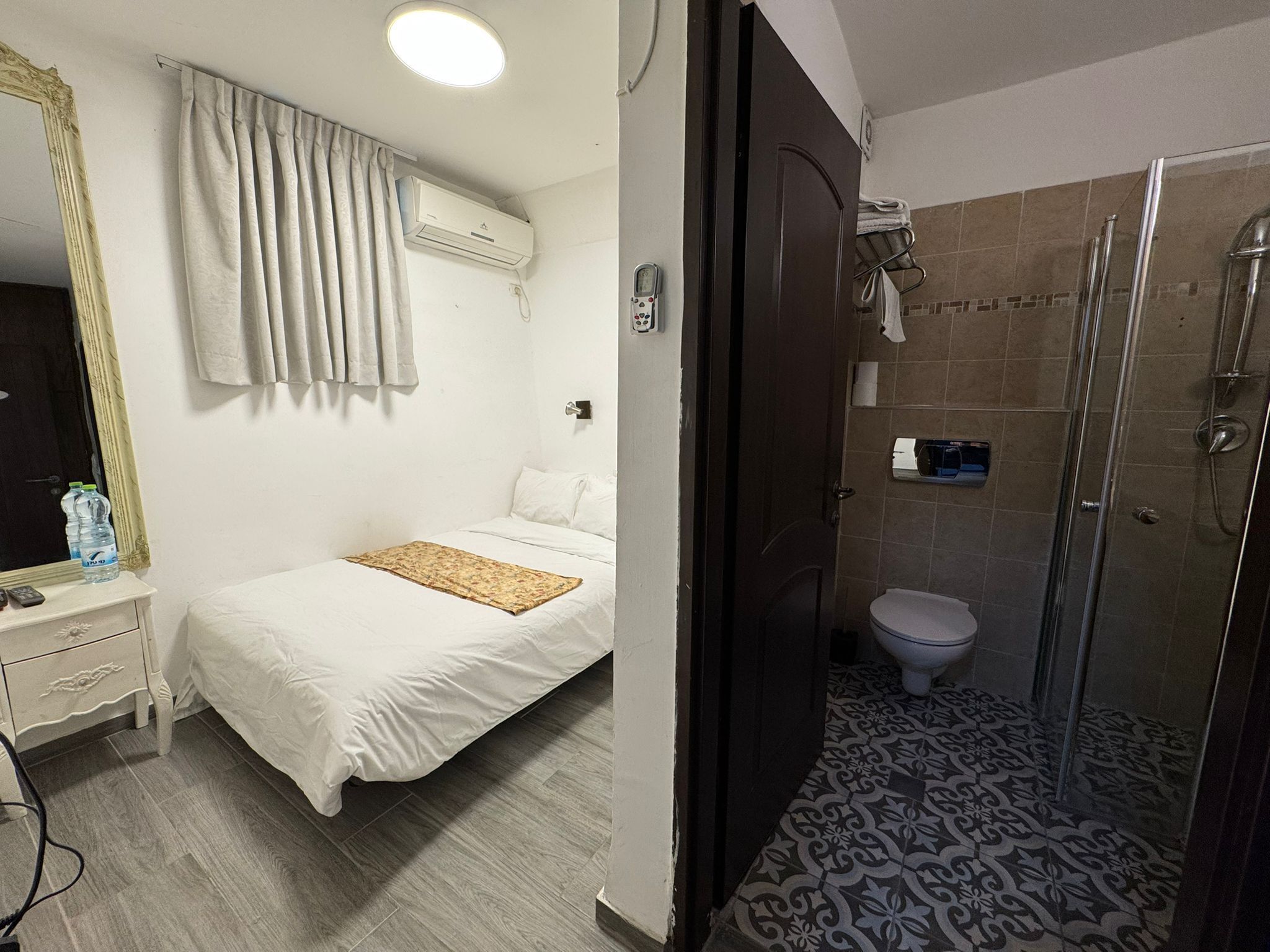 Una habitación de hotel con cama, mesita de noche y zona de ducha.