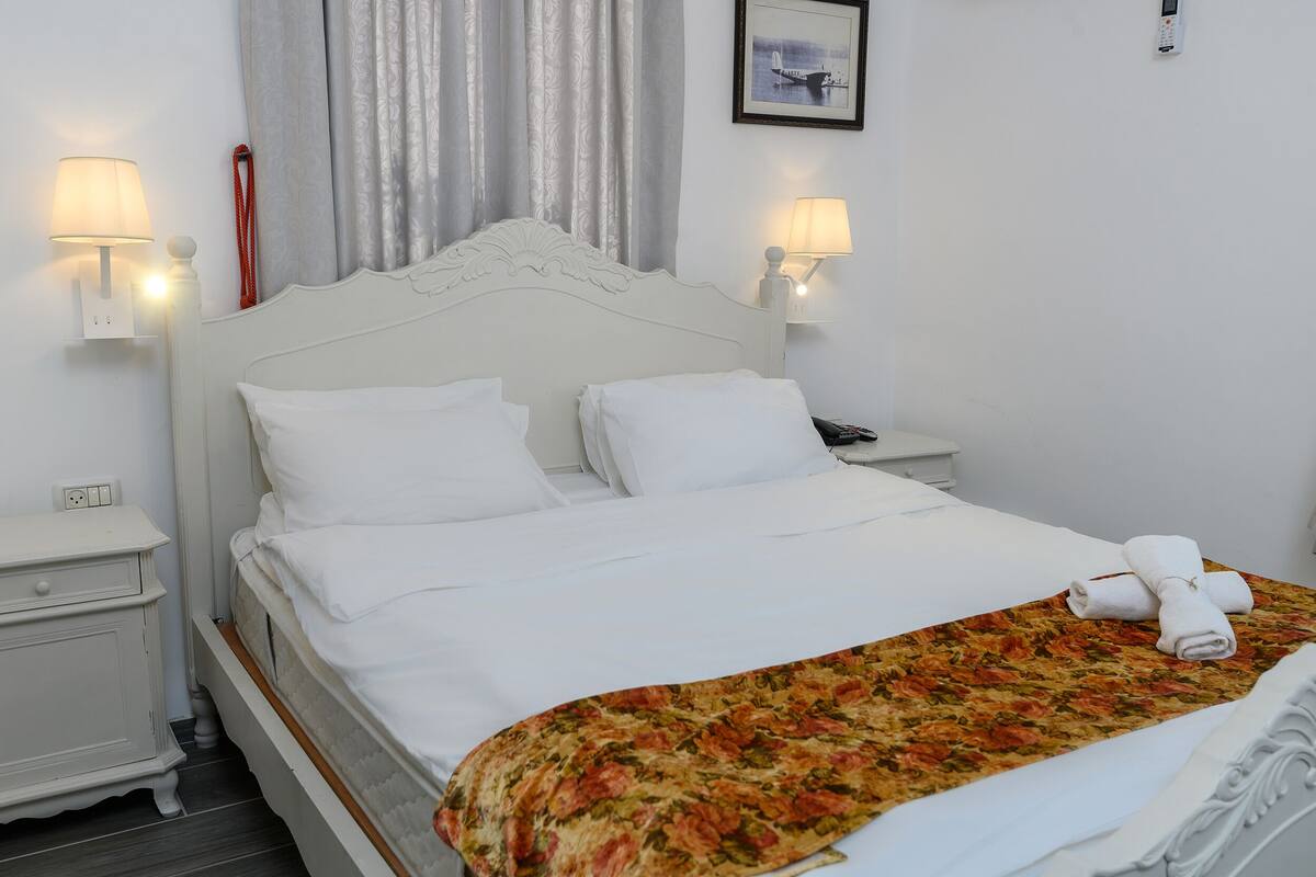 A neatly made bed with white linens and a floral bedspread, two bedside lamps, and a framed picture on the wall.