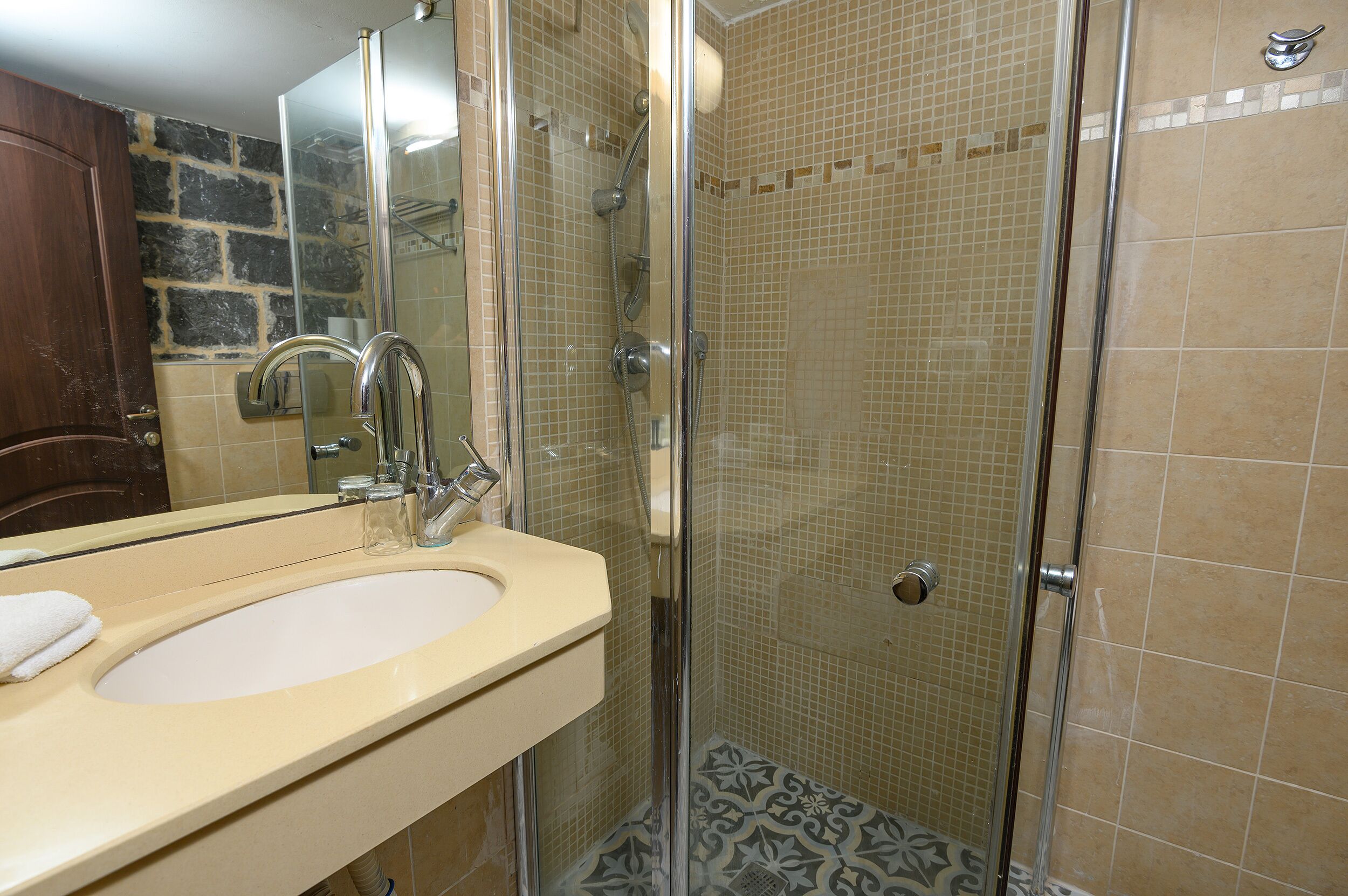 A bathroom with a beige sink, a mirror, and a shower with a glass door.