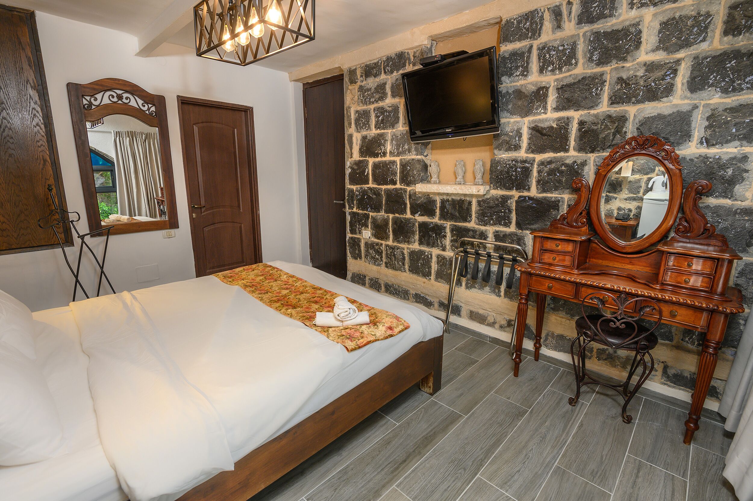 A bedroom with a bed, a dresser, a mirror, and a television mounted on a stone wall.
