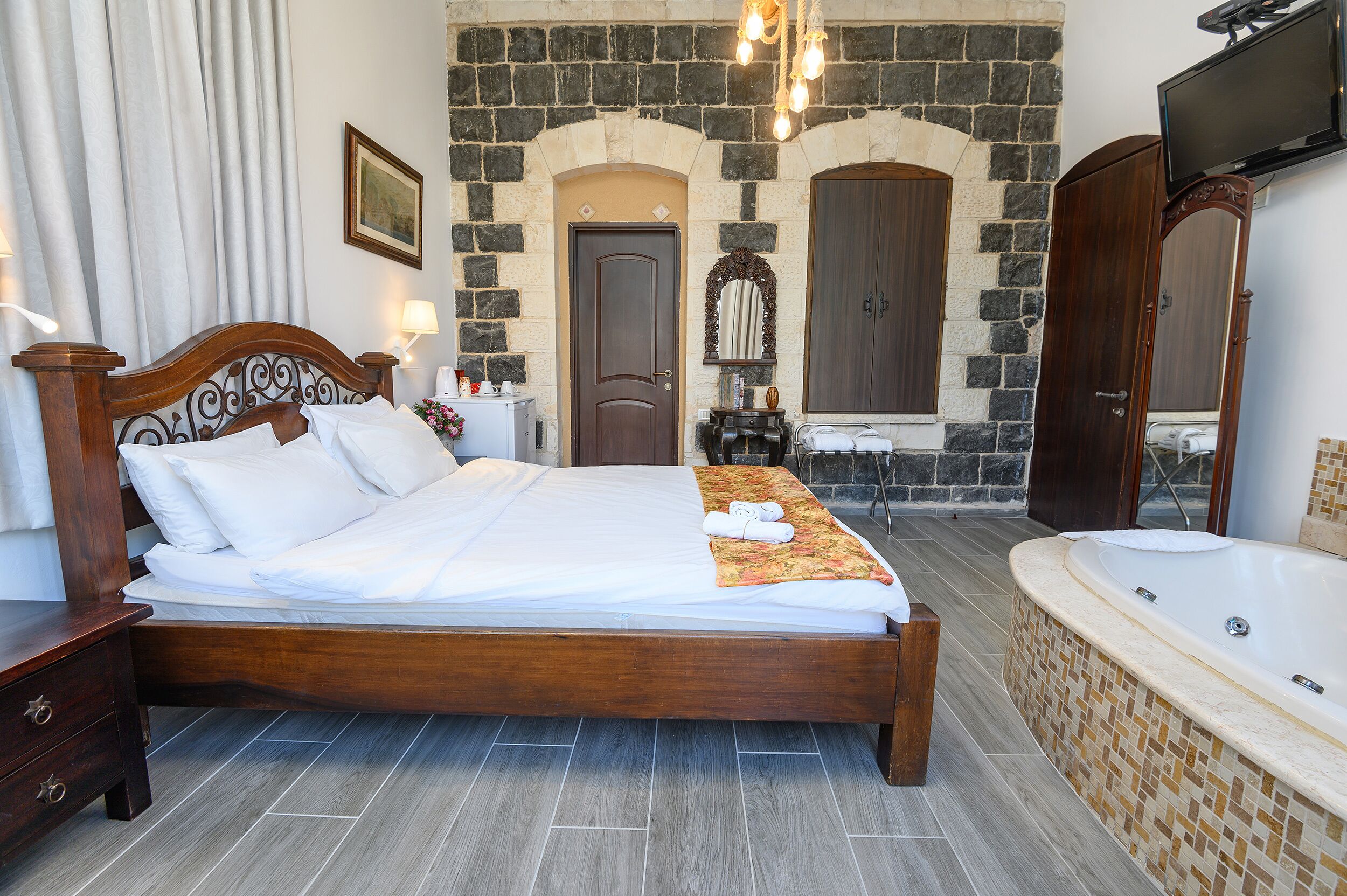 A spacious bedroom with a large bed, a built-in bathtub, and a stone wall.